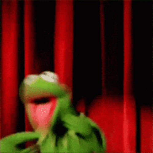 Kermit The Frog Is Standing Behind A Red Curtain . GIF