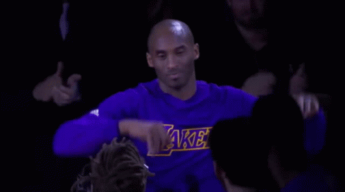 Kobe Bryant Is Wearing A Purple Lakers Shirt While Sitting In The Stands During A Game . GIF