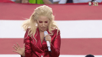 Lady Gaga Is Singing Into A Microphone While Wearing A Red Jacket . GIF