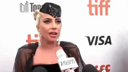 Lady Gaga Is Wearing A Hat And Holding A Microphone While Talking To A Reporter . GIF