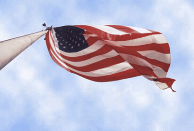 Large American Flag Flying Against Blue Sky GIF