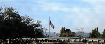 Large American Flag Flying In Front Of Building GIF