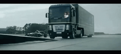 Large Black Truck Driving Next To Race Car GIF