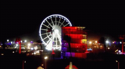 Large Ferris Wheel Lit Up At Night In Front Of Building GIF