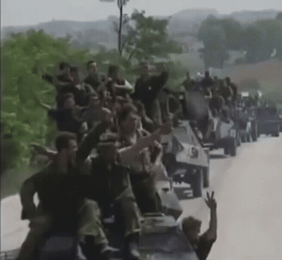 Large Group Sitting On Military Vehicles On Road GIF