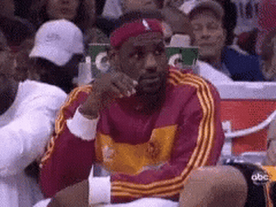 Lebron James Is Sitting In The Stands At A Basketball Game Wearing A Headband And A Red Jacket . GIF