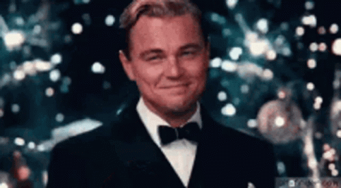 Leonardo Dicaprio Is Wearing A Tuxedo And Bow Tie And Smiling In Front Of A Christmas Tree . GIF