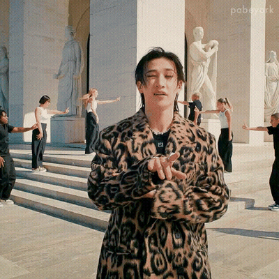 Leopard Coat Man Holding Microphone To Ponytail Woman GIF