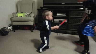 Little Boy Holding Red Lightsaber In Front Of TV GIF