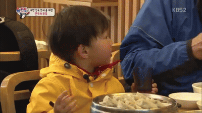 Little Boy In Yellow Jacket Sitting At Table With Bowl Of Food And KB52 Logo GIF