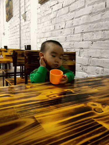 Little Boy Sitting At Table With Cup GIF