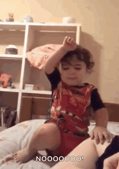Little Boy Sitting On Bed Hand Up GIF