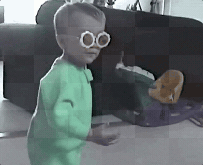 Little Boy With Glasses And Green Outfit Beside Couch GIF