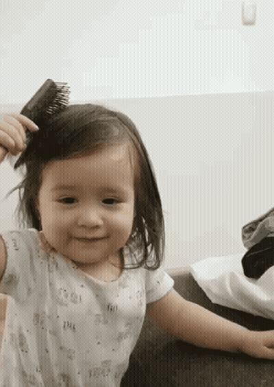 Little Girl Brushing Hair And Smiling GIF