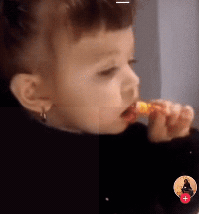 Little Girl Eating Yellow Lollipop With Red Plus Sign GIF