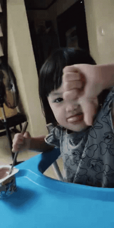 Little Girl Eating Yogurt With Spoon Giving Thumbs Down GIF