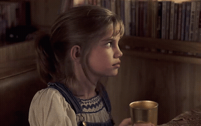 Little Girl Holding Cup In Front Of Bookshelf GIF