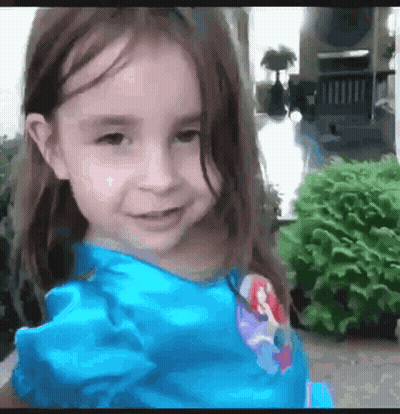 Little Girl In Blue Dress Smiling In Front Of House GIF