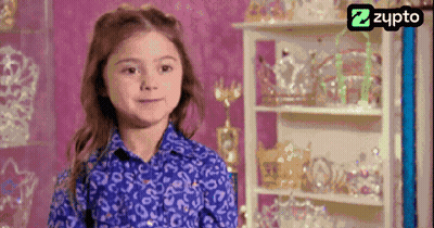 Little Girl In Blue Shirt Smiling In Front Of Crown Shelf GIF