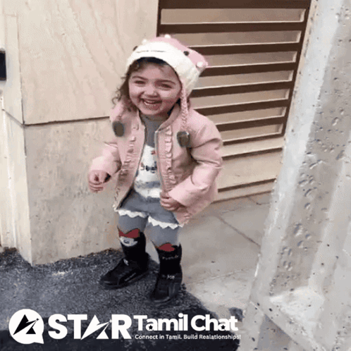 Little Girl In Pink Jacket And Hat In Front Of Tamil Chat Sign GIF