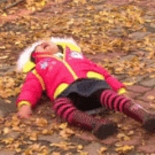 Little Girl In Red Jacket Laying On Ground Covered In Leaves GIF