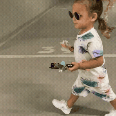 Little Girl In Sunglasses And Floral Outfit Walking In Parking Lot GIF