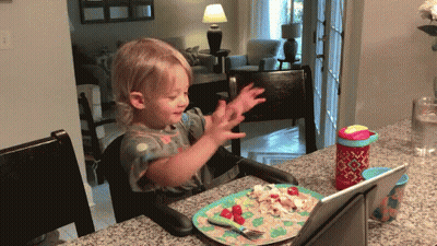 Little Girl Sits At Table With Plate Of Food GIF