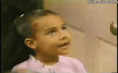 Little Girl Sitting In Front Of Door Looking At Camera GIF