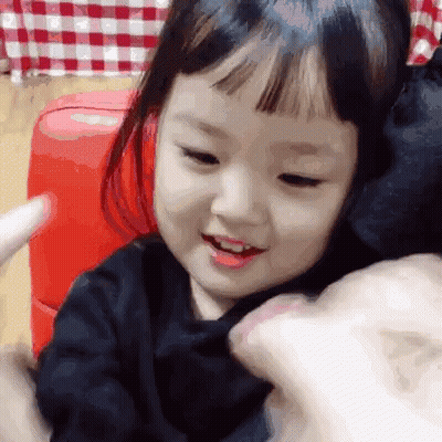 Little Girl Smiling On Red Couch Held By Person GIF