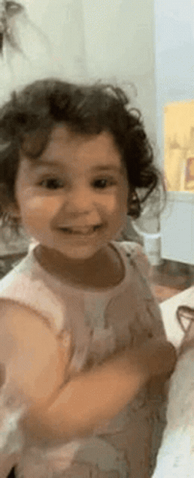 Little Girl With Curly Hair Smiling In Kitchen GIF