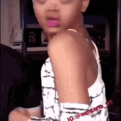 Little Girl With Pink Lipstick Sitting In Chair Looking At Camera GIF