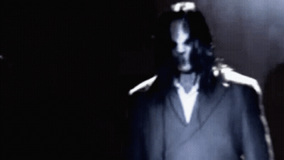 Long-Haired Man In Suit Standing In Dark GIF