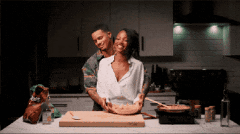 Man And Woman Cooking Together With Bag Of Doritos In Background GIF