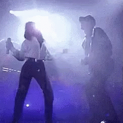 Man And Woman Dancing On Stage With Purple Lights GIF