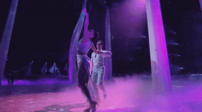 Man And Woman Dancing On Stage With Purple Lights GIF