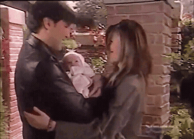 Man And Woman Holding Baby In Front Of Brick Building GIF