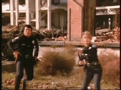 Man And Woman Holding Guns At Destroyed Building GIF