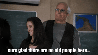 Man And Woman In Front Of Chalkboard Saying Sure Glad There Are No Old People Here GIF