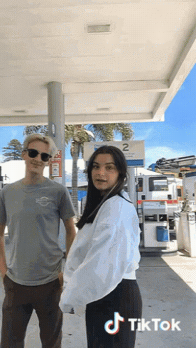 Man And Woman In Front Of Gas Station Sign 2 GIF
