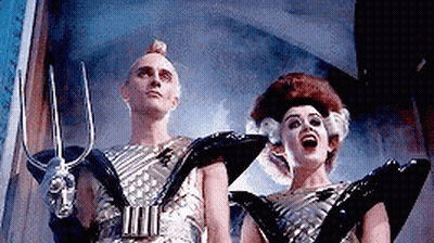 Man And Woman In Futuristic Costumes Holding Trident GIF