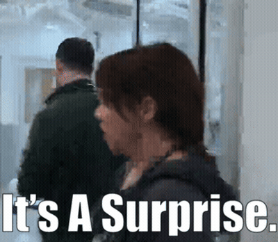 Man And Woman In Hallway Saying It's A Surprise GIF