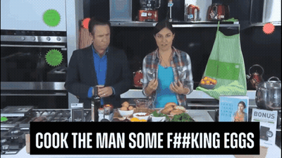 Man And Woman In Kitchen With Sign Saying Cook The Man Some F##king Eggs GIF