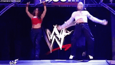 Man And Woman Jumping On Stage In Front Of Wrestling Logo GIF