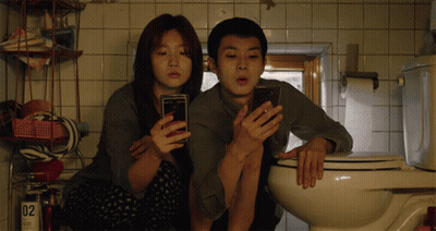 Man And Woman Looking At Phones In Bathroom GIF