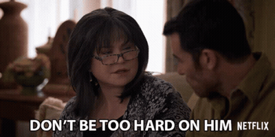 Man And Woman On Couch Woman Says Don't Be Too Hard On Him GIF