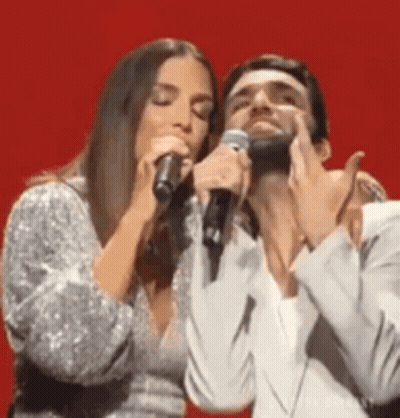 Man And Woman Singing Into Microphones On Stage GIF
