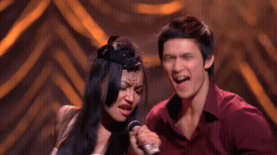 Man And Woman Singing Into Microphones On Stage GIF