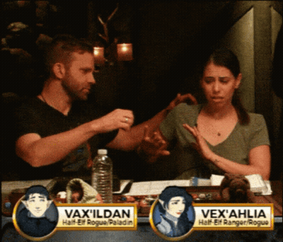 Man And Woman Sitting At Table With Vax Ildan Sign GIF