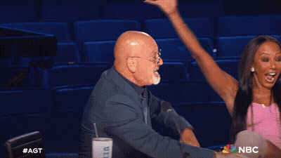 Man And Woman Sitting In Front Of AGT Sign GIF