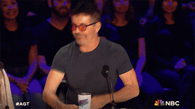 Man And Woman Sitting In Front Of AGT Sign GIF